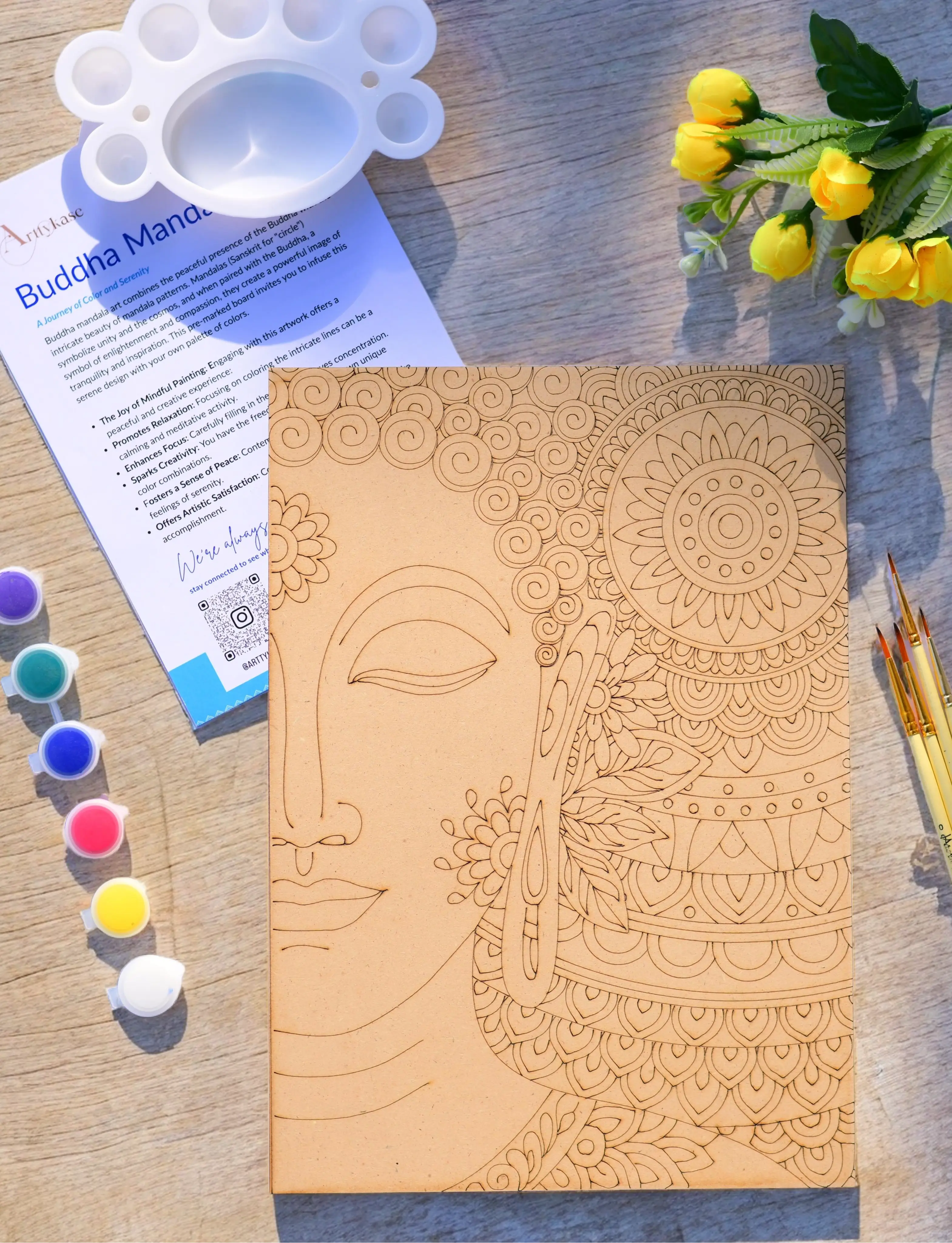 Buddha mandala pre-drawn wooden board surrounded by acrylic paint bottles, fine brushes and palette on a natural wood surface - Arttykase DIY art kit