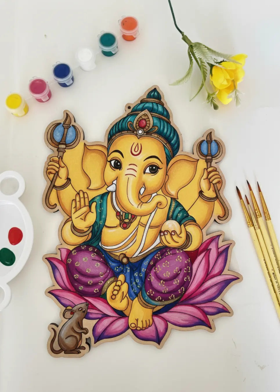 Lord Ganesha DIY art kit contents flat lay - pre-drawn board with Ganesha on pink lotus, acrylic paints and brushes on white background - Arttykase