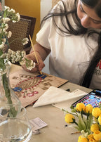 Woman painting a Lord Krishna Pichwai devotional art design at a table with flowers - Arttykase Indian folk art mindfulness kit for beginners