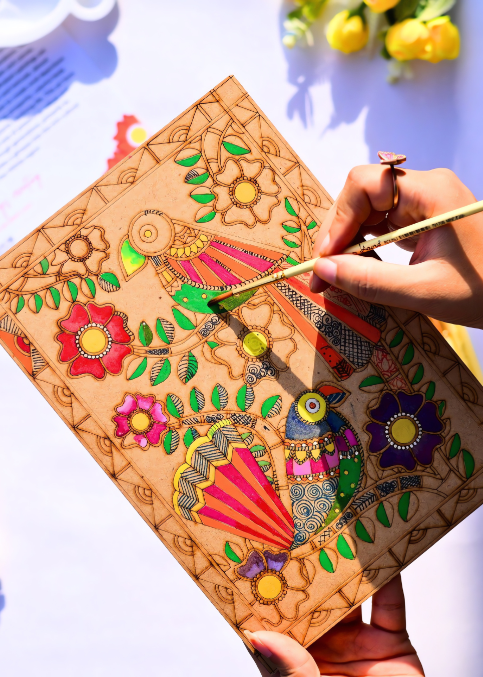 ands painting a vibrant Madhubani bird folk art design in progress on a pre-etched A4 MDF wooden board - colorful birds, flowers and leaves in traditional Indian folk art style - Arttykase DIY painting kit