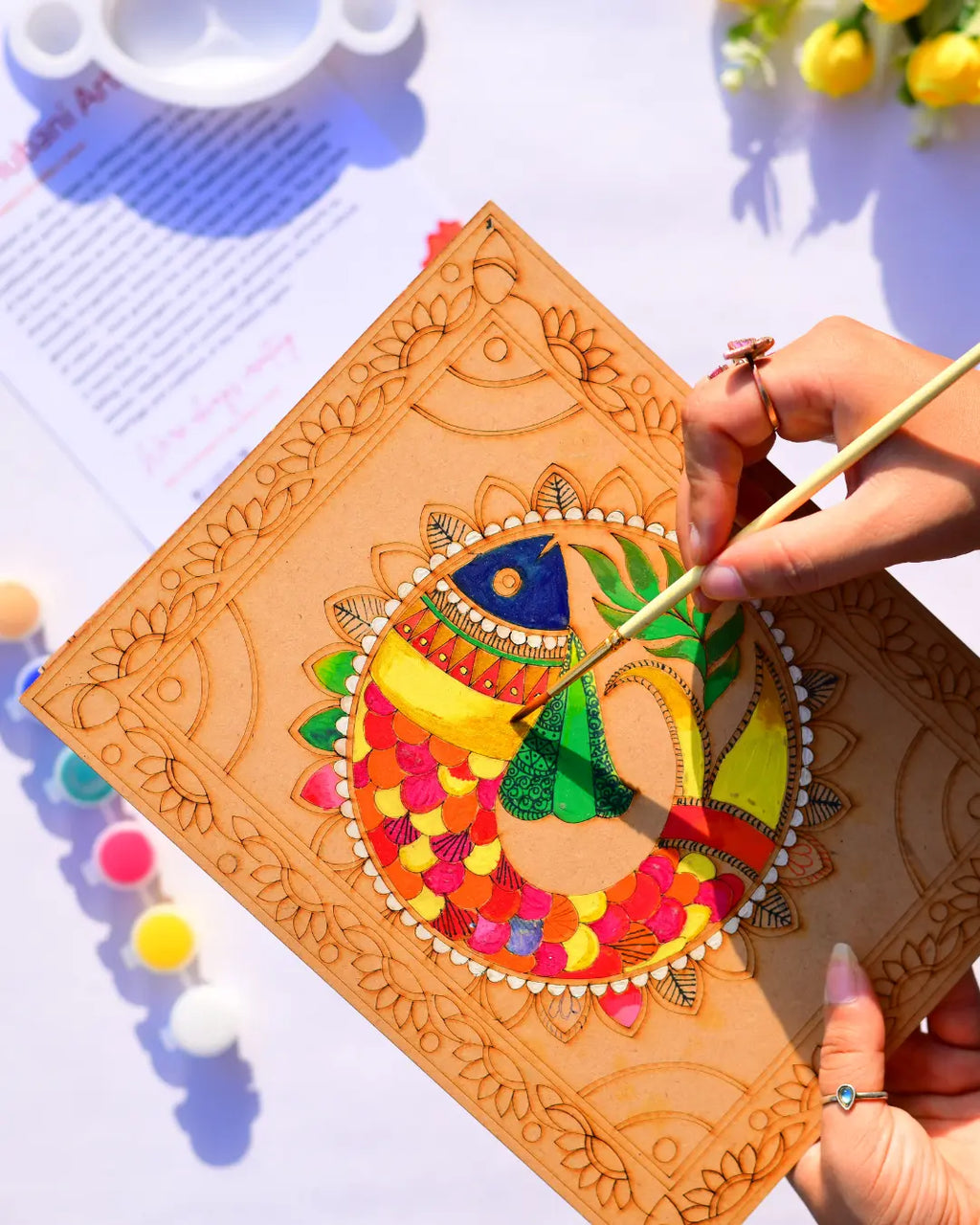 Hand painting a Madhubani good luck fish mandala design on a pre-drawn wooden board with a fine brush and vibrant acrylic paints - Arttykase Indian folk art kit USA